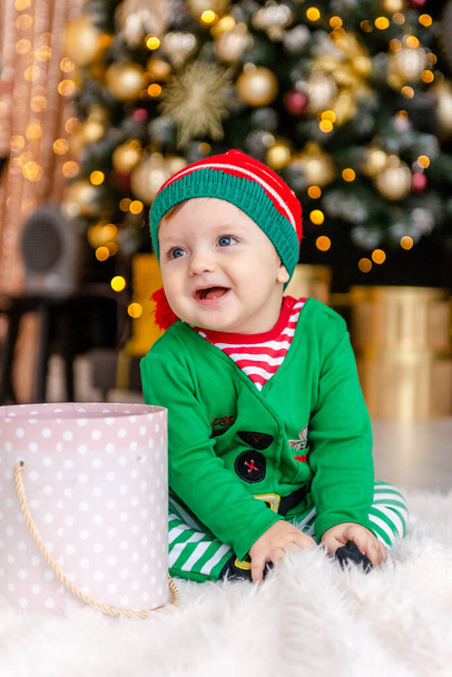 A cute little boy dressed as an elf opens a Christmas present in a decorated Christmas house. - Foto, imagen