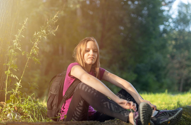 rest while hiking. young caucasian woman hiker sitting in forest relaxing during hike. woman with backpack. - Photo, image