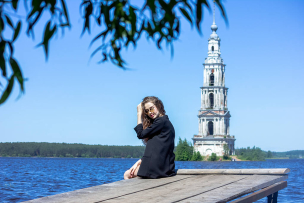 A girl in a black jacket against the background of the Uglich reservoir Kalyazin city. Rocky shore. - Foto, Imagen