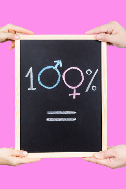 Frau und Mann halten ein Dünenbrett mit dem zu 100% gleichen Symbol auf rosa Hintergrund. Konzept der Gleichheit - Foto, Bild