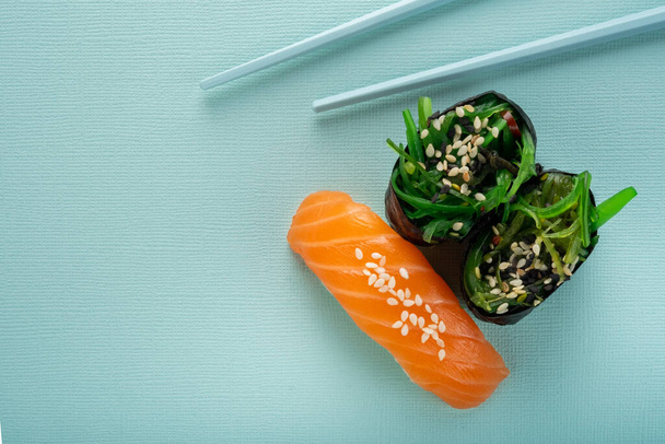 Dvě mořské řasy Sushi Chuka a sushi nigiri s lososem s hůlkami na modrém pozadí - Fotografie, Obrázek