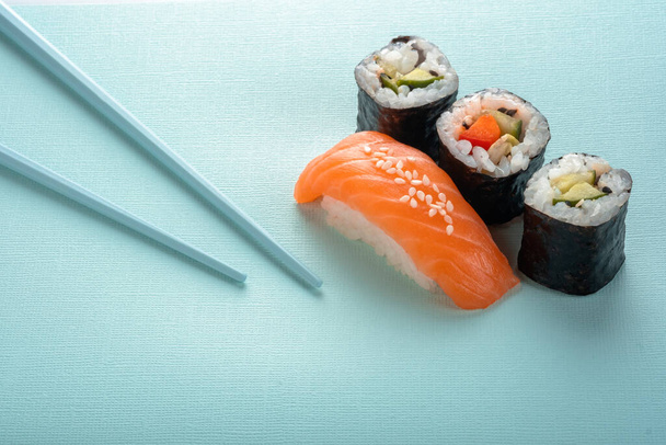 Set di sushi con nigiri di salmone e involtino con cetriolo e verdure con bacchette su fondo blu, per il menu del sushi bar - Foto, immagini