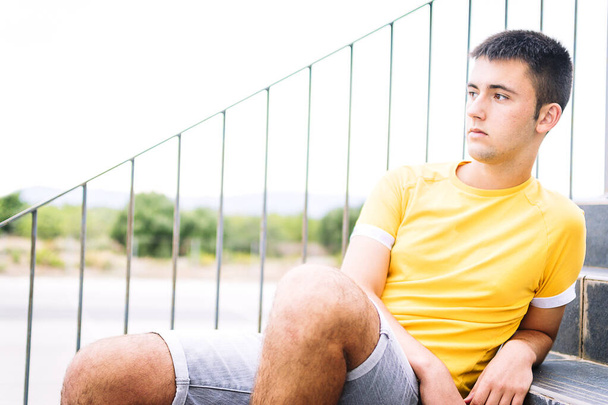 Подросток, сидящий на лестнице в желтой футболке - Фото, изображение