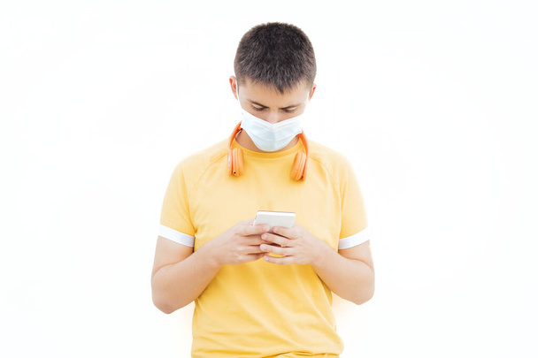 Adolescent avec masque médical attendant appuyé sur le mur avec t-shirt jaune - Photo, image