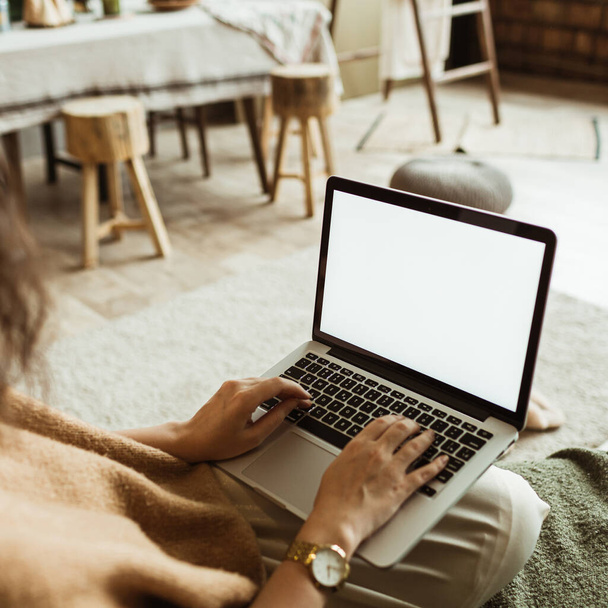 Jonge vrouw werken op laptop met lege display scherm met mockup kopieerruimte. Moderne woonkamer interieur. Werkzaamheden thuis. - Foto, afbeelding