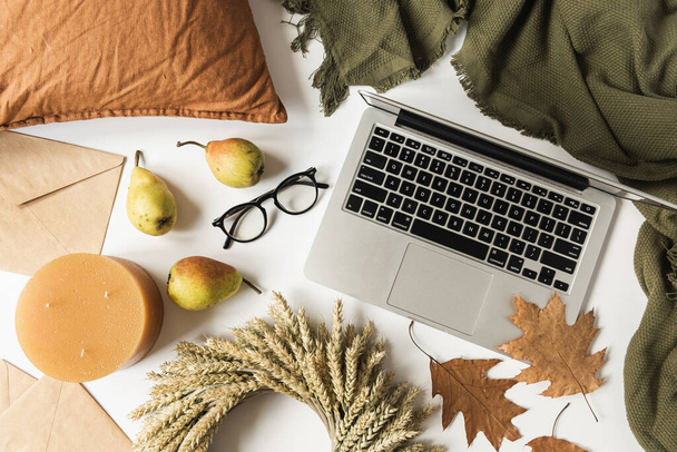 ノートパソコン、メガネ、麦藁の花輪、乾燥した秋の葉、梨、毛布、枕、封筒付きのホームオフィステーブルデスクワークスペース。秋のコンセプト。平敷. - 写真・画像