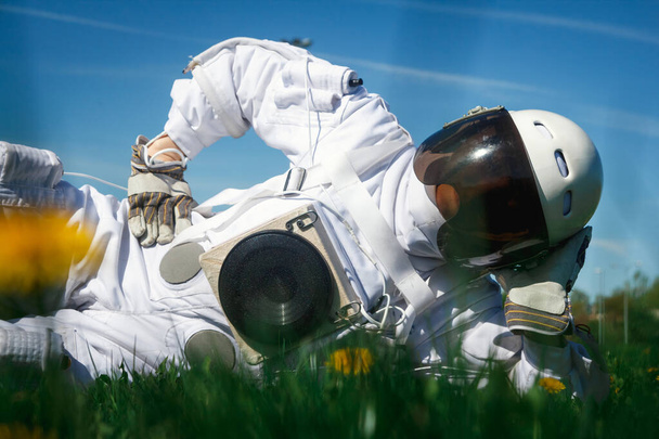 ヘルメットの未来型宇宙飛行士は花の間の緑の芝生の上に座っている. - 写真・画像