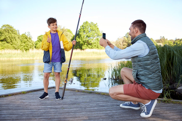 father photographing son with fishing rod on river - Foto, Imagem