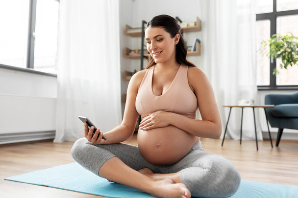 happy pregnant woman with phone doing yoga at home - Foto, Imagem