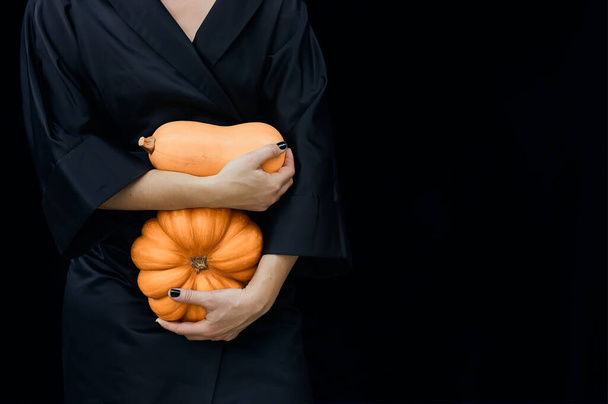 Woman in black silk kimono holds pumpkins on dark background. Space for text. Autumn holiday, Celebration design. - Photo, Image