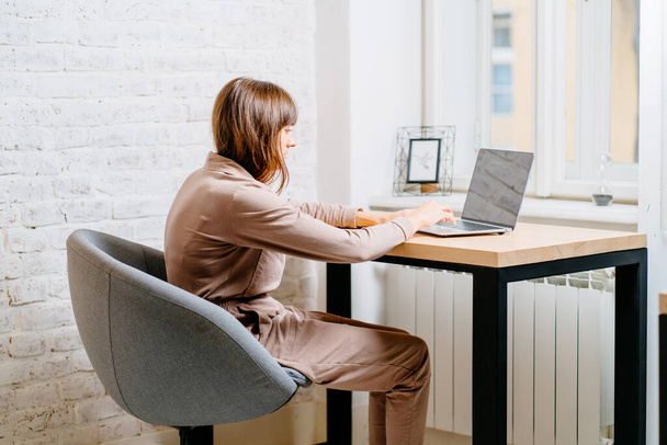 Die richtige Haltung bei der Arbeit am Computer. Eine Frau sitzt an einem Tisch mit einem Laptop. Wirbelsäulenverkrümmung. Gute Haltung. Gesunder Rücken. - Foto, Bild