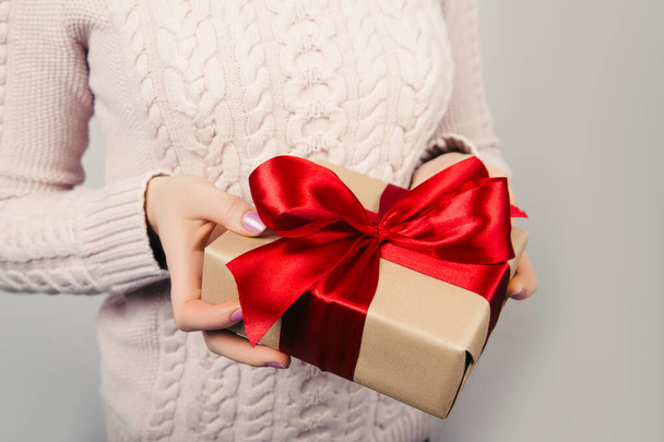 Woman's hands in pink jumper holding craft paper gift box with a present for Christmas, new year, valentine day or anniversary on black background, top view - Photo, Image