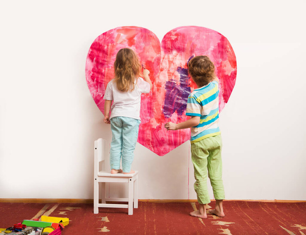 two children draw paints heart on a wall. Happy family day concept - Foto, immagini