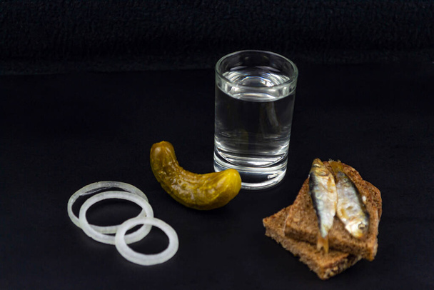 ウォッカのグラス、パン2個、黒の背景にキュウリの漬物 - 写真・画像