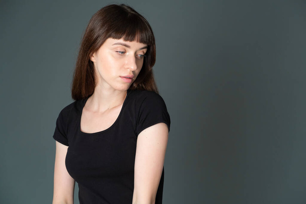 Studio portrait of a pretty brunette woman in a black t-shirt, turned away, against a plain grey background, looking at camera - Foto, afbeelding