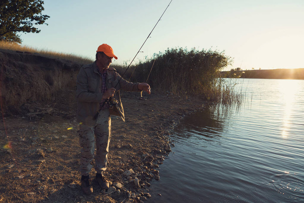 Pescador de pie en la orilla del río y tratando de atrapar un pez. Deporte, recreación, estilo de vida. - Foto, imagen