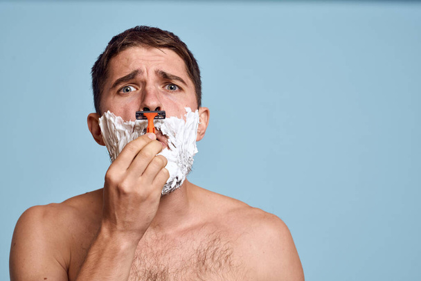 Homme avec rasoir et mousse blanche sur son visage fond bleu procédures de bain torse nu - Photo, image