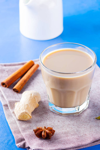 Masala chai tea on a linen napkin. Traditional indian drink - masala tea with various spices. Glass of masala tea on a blue background - Fotó, kép