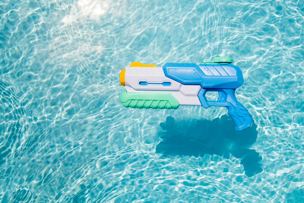 A child's blue water gun floats in the pool. A toy for playing in the pool or on the beach - Фото, изображение