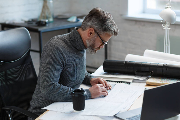 Interior designer working in office with blueprints.Engineer inspect architectural plan, sketching a construction project.Portrait of handsome bearded man at workplace. Business construction concept - Valokuva, kuva