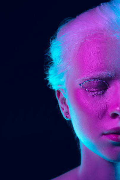 Portrait of beautiful albino girl isolated on dark studio background in neon light - Zdjęcie, obraz