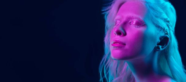 Portrait of beautiful albino girl isolated on dark studio background in neon light - 写真・画像