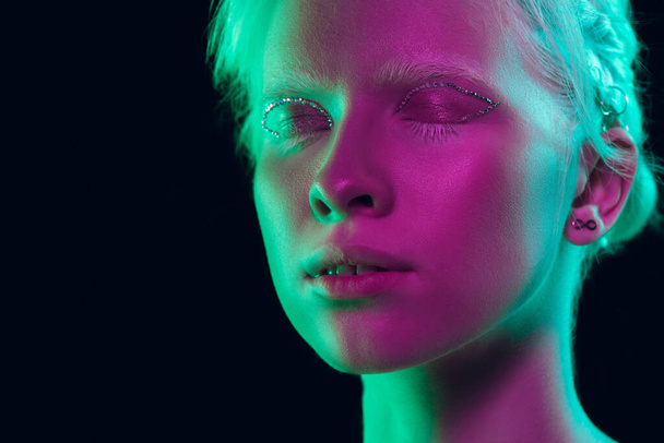 Portrait of beautiful albino girl isolated on dark studio background in neon light - Фото, изображение