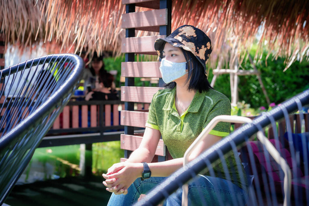 Asiatische Frau trägt eine Schutzmaske ist entspannend und denkt an eine gute Zeit mit grünem Hintergrund während des Coronavirus Ausbruch covid-19 Pandemie einen neuen normalen Lebensstil. Gesundheitsfürsorge und soziale Distanzierung - Foto, Bild
