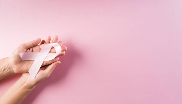 Mains tenant des rubans roses, sensibilisation au cancer du sein, noeud symbolique sensibilisant la couleur sur la tumeur du sein des femmes. Soins de santé et concept médical. - Photo, image