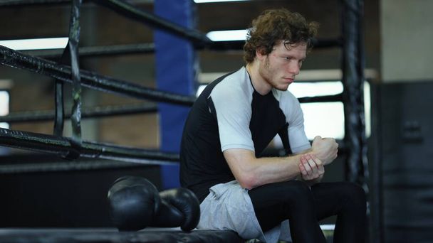 Sad fighter sitting in fitness center. Kickboxer waiting for fight at gym - Fotó, kép