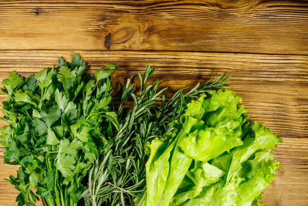 Čerstvě zelená petržel, listy salátu a rozmarýnové bylinky na dřevěném stole. Horní pohled - Fotografie, Obrázek