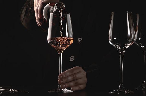 Sommelier pouring rose wine into glass at wine tasting in winery, bar or restaurant. Dark background - Foto, Bild