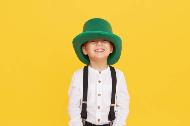 Smiling little child boy in green leprechaun hat on yellow background. St. Patrick Day celebration. Funny face - Photo, Image