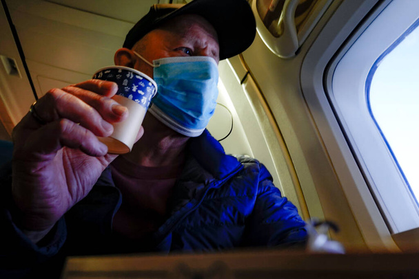 Un pasajero de línea aérea con una máscara al lado de la ventana. - Foto, Imagen