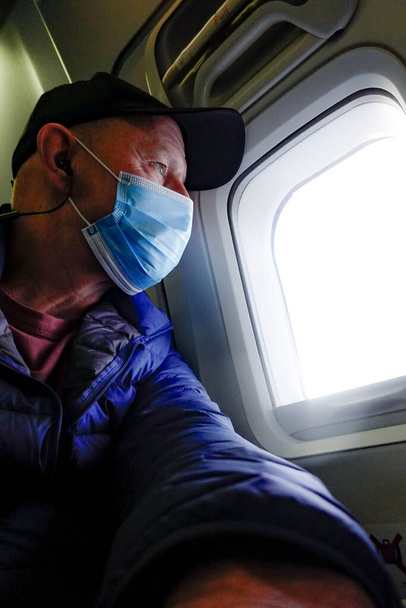 Un passeggero della compagnia aerea che indossa una maschera vicino alla finestra. - Foto, immagini