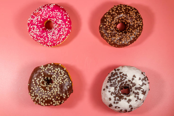 Вкусные пончики на розовом фоне. Вид сверху - Фото, изображение