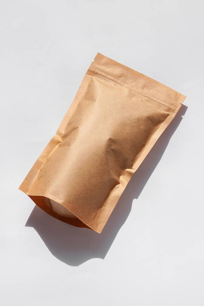 白い背景に影が隔離されたコーヒー豆のトップビューと茶色のクラフト紙ポーチバッグ。食品や商品テンプレートのモックアップのためのパッケージ。茶葉用クラスプ付きパック、重量物フラットレイ - 写真・画像