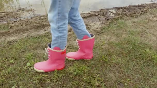 Holčička v deštivých botách v chladném dni u jezera - Záběry, video