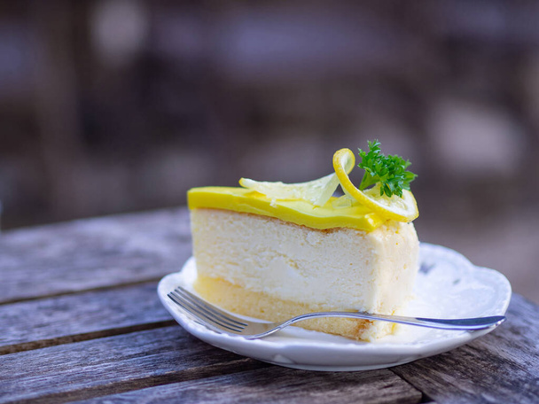 Boční pohled na krájený citrónový dort na bílém talíři na dřevěném stole v zahradě. - Fotografie, Obrázek