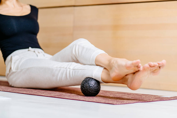 Unrecognisable woman using massage ball for muscle soreness after fitness exercise, muscle strain after high-intensity workouts, and physical and mental exertion after sitting in the office. - Photo, Image