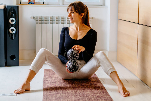 Medioevo sportivo bruna donna allenatore seduto su tappetino yoga e mostrando palla da massaggio, duoball per il rilascio miofasciale exircise, superare il dolore, concetto di riabilitazione. - Foto, immagini