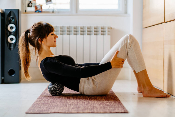 Side view of woman in sportswear using duoball for myofascial release exercise for spine lying on yoga mat at home or office, overcome pain, rehabilitation concept. - Photo, Image