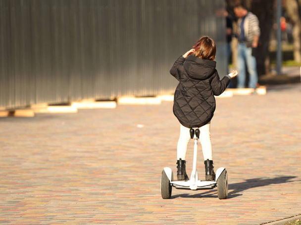 Ένα κορίτσι ιππεύει στο πάρκο με ένα γυροσκόπιο και μιλάει στο τηλέφωνο. Σύγχρονος ηλεκτροοικολογικός τρόπος μεταφοράς. Οικολογία στην πόλη. Δραστηριότητα των παιδιών. Αθλητικά για την υγεία. Να είστε σε θέση να κρατήσει balanc σας. - Φωτογραφία, εικόνα