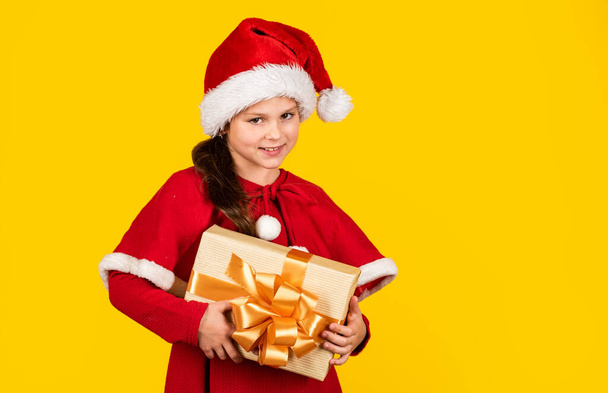 Wish list concept. My happy day. Xmas gift shopping. Little girl Santa hat hold gift box. Kid hold present box yellow background. Gift package. Merry Christmas and happy holidays. Winter holidays - Φωτογραφία, εικόνα
