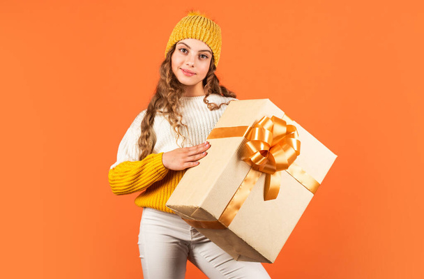 What is inside. winter holiday surprise. small girl knitted hat and sweater. kid hold present box orange background. happy new 2020 year. gift delivery service. shopping advantages. christmas is here - Photo, Image