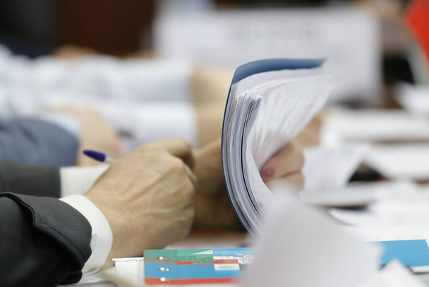 Egy öltönyös férfi töltőtollat tart a kezében. Üzleti papírok, mappák és jegyzetfüzetek vannak az asztalon. - Fotó, kép