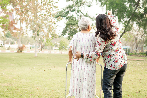 Βοήθεια και φροντίδα της Ασίας ανώτερος ή ηλικιωμένη ηλικιωμένη γυναίκα χρησιμοποιούν περιπατητής με ισχυρή υγεία, ενώ το περπάτημα στο πάρκο σε χαρούμενες φρέσκες διακοπές.  - Φωτογραφία, εικόνα