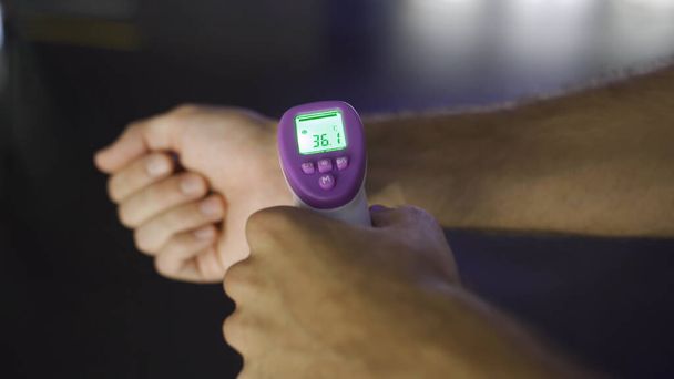 他の人の温度計で温度を測定人。メディア。コロナウイルス予防のための非接触赤外線温度計を使用して男性の手の閉じる. - 写真・画像
