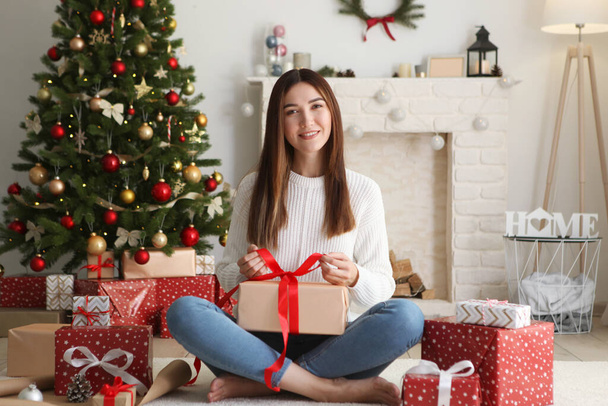 Young beautiful girl packing christmas gifts in decorated home interior - Fotó, kép