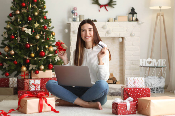 Young beautiful woman is shopping for christmas in festive interior at home - Photo, Image